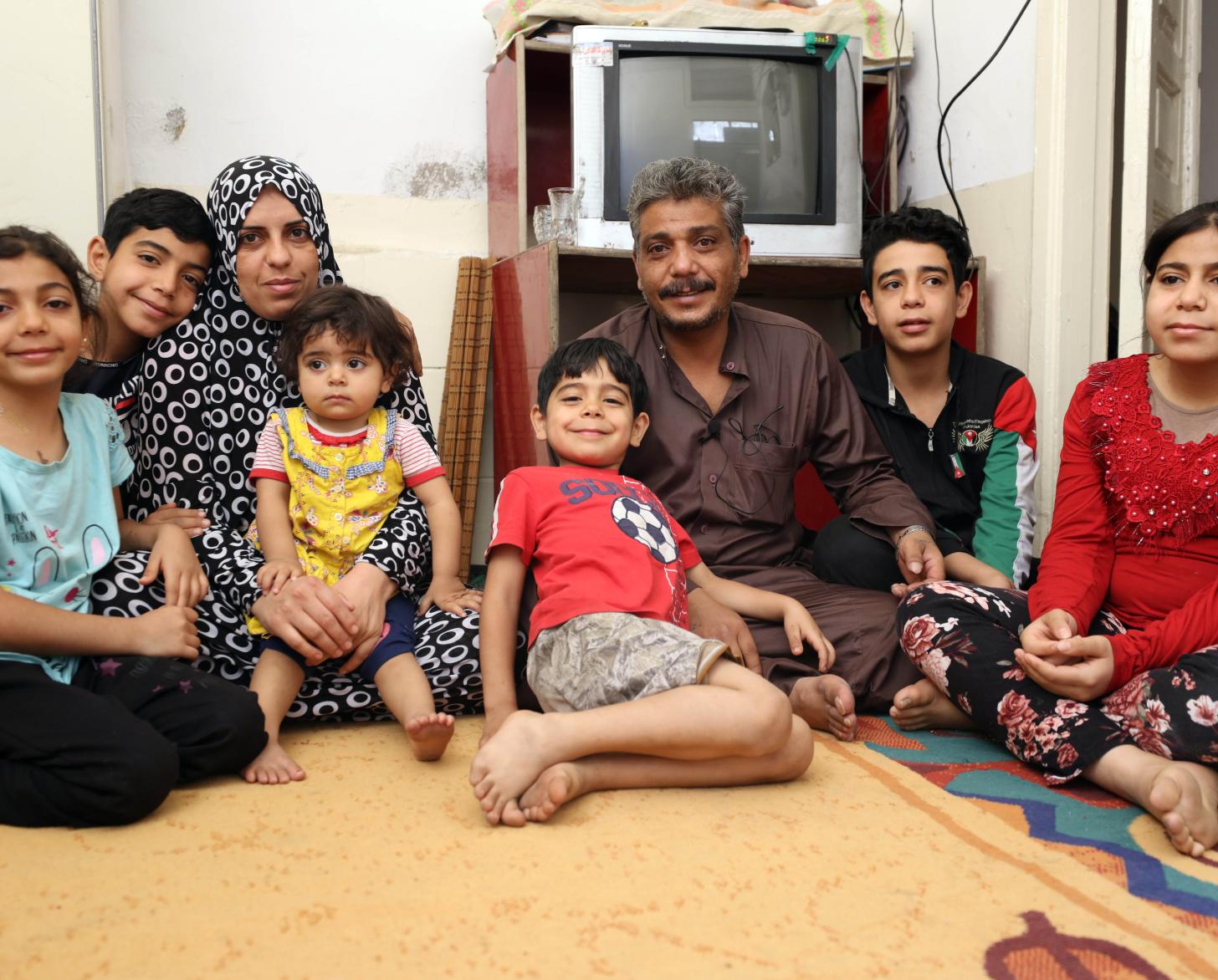 Khaled sits in their tv room on the floor with his family surrounding him.