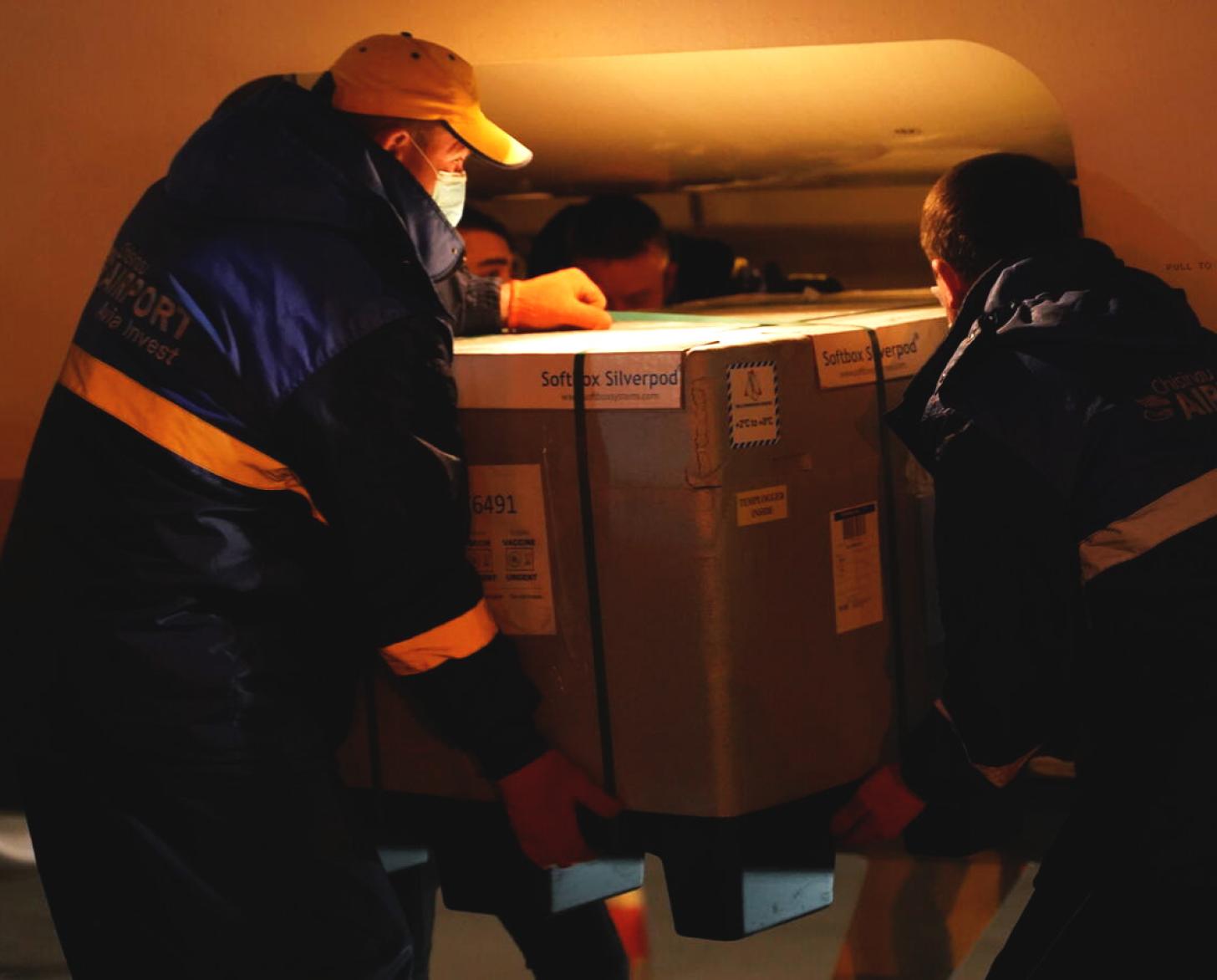Two airport employees unload a crate of vaccines from the plane's cargo space.