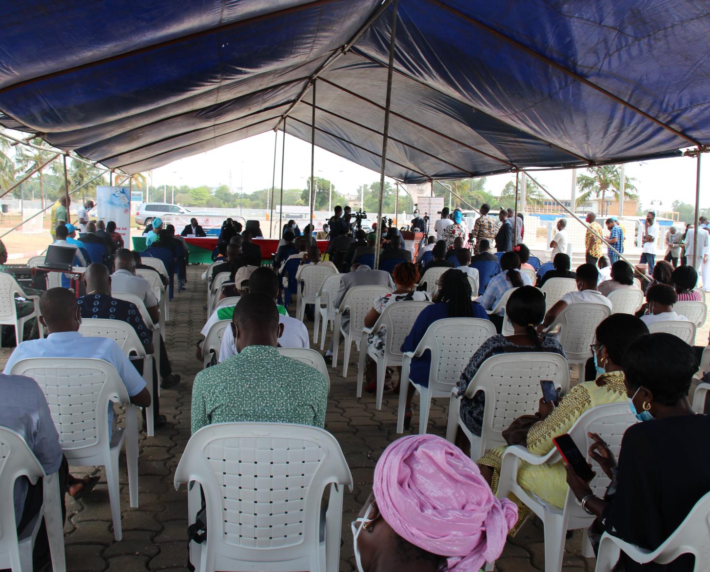 يجلس العديد من الأشخاص المتباعدين اجتماعيًا تحت خيمة في الهواء الطلق.