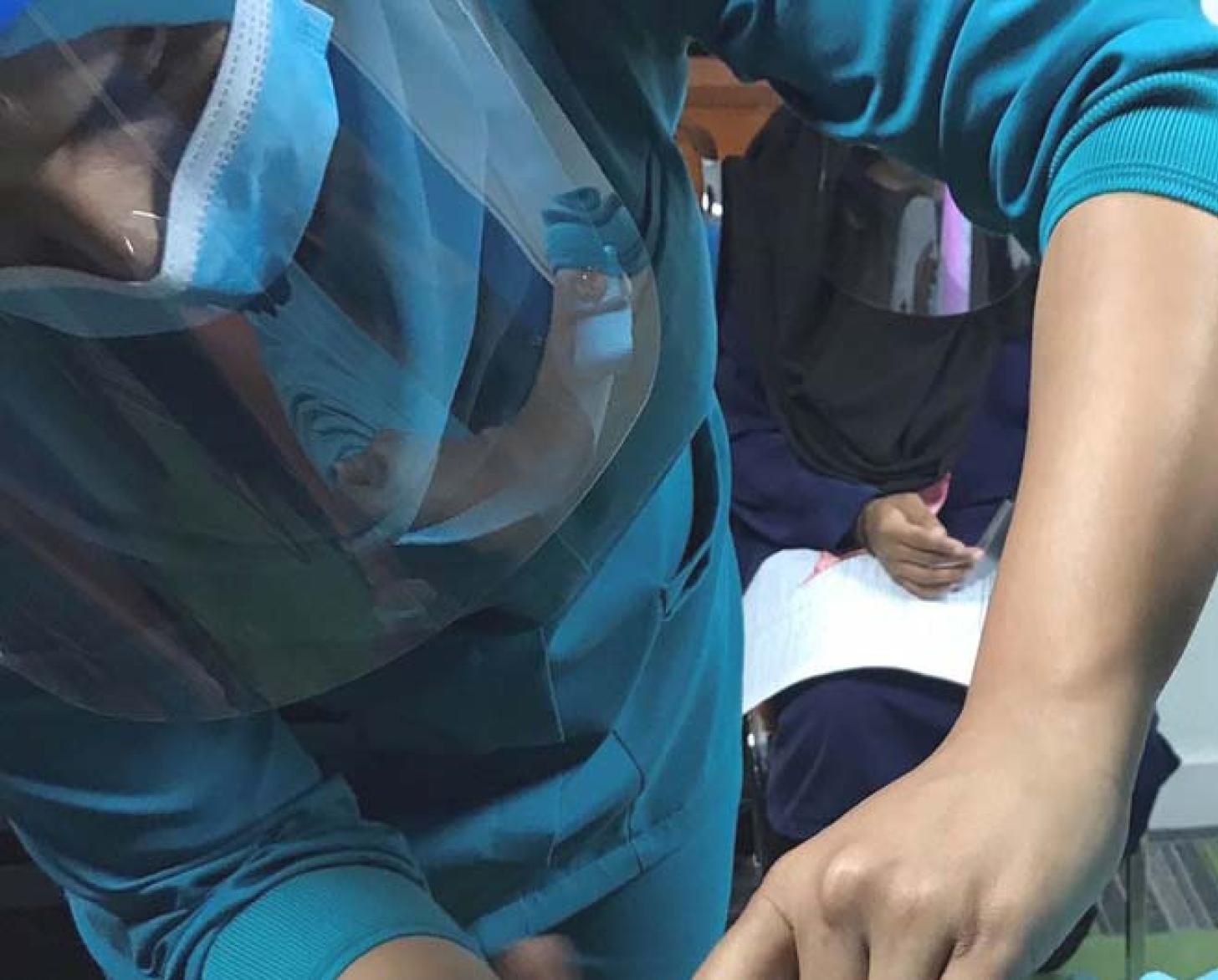 Une homme en tenue médicale et portant un masque et une visière de protection administre un vaccin à un patient portant un masque.