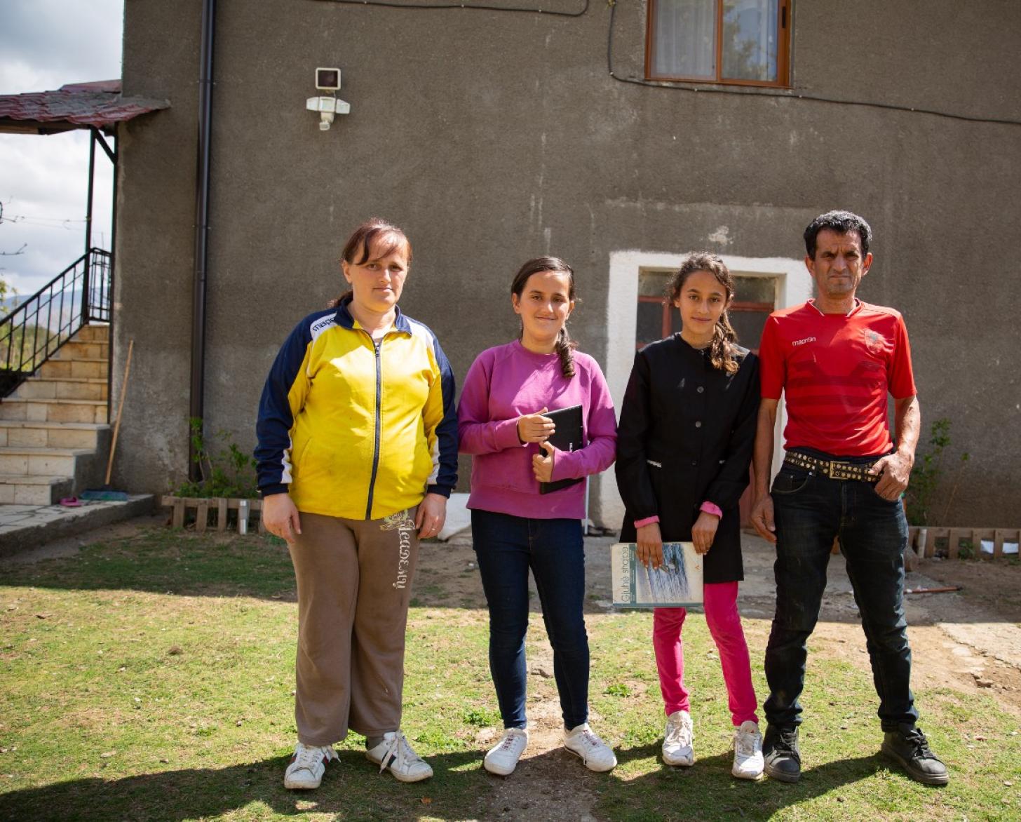 Una familia de cuatro miembros, entre ellos un hombre, una mujer y dos hijas, están parados frente a un edificio.