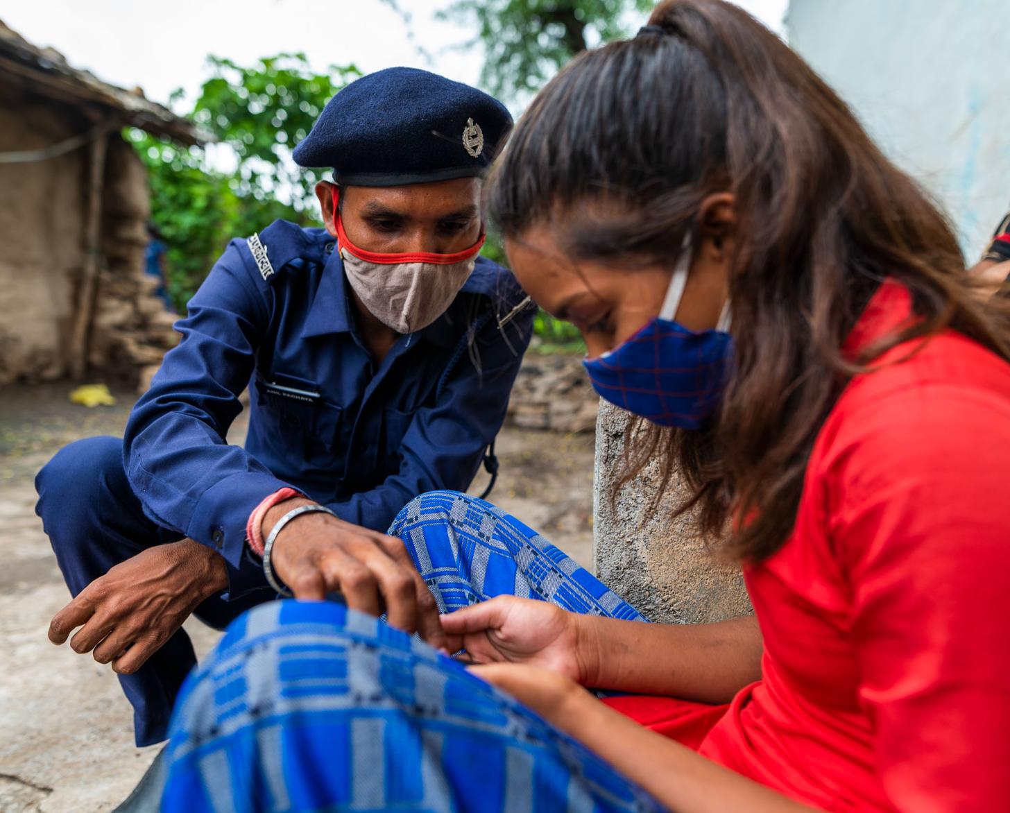 一个身着军装的人跪在一个正在看手机的女人旁边。