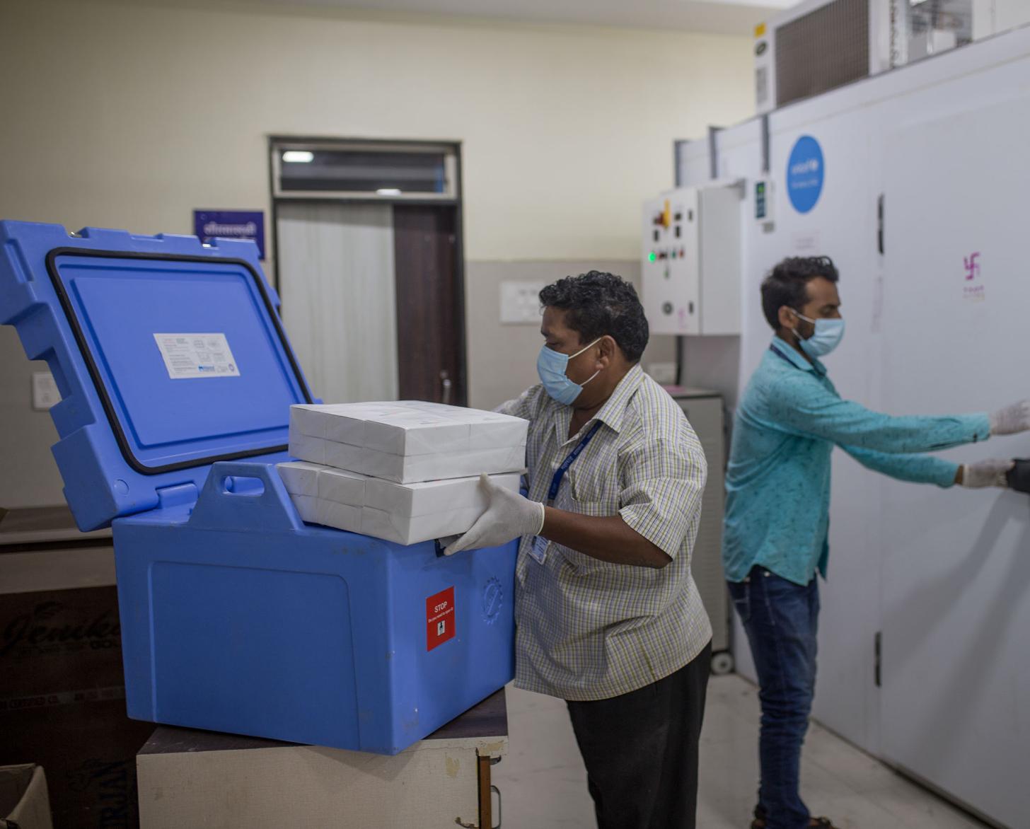 两名医务人员站在大冰箱旁边，怀里抱着新冠疫苗。