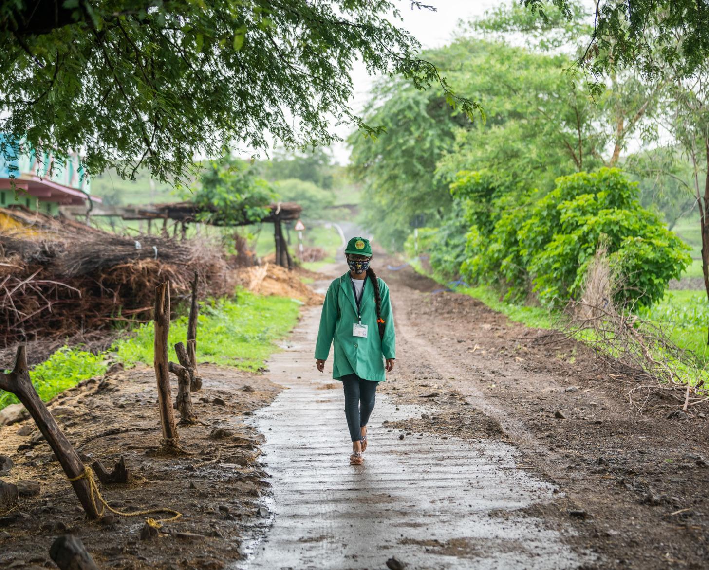 一个穿着绿色夹克的人走在一条泥泞的路上。