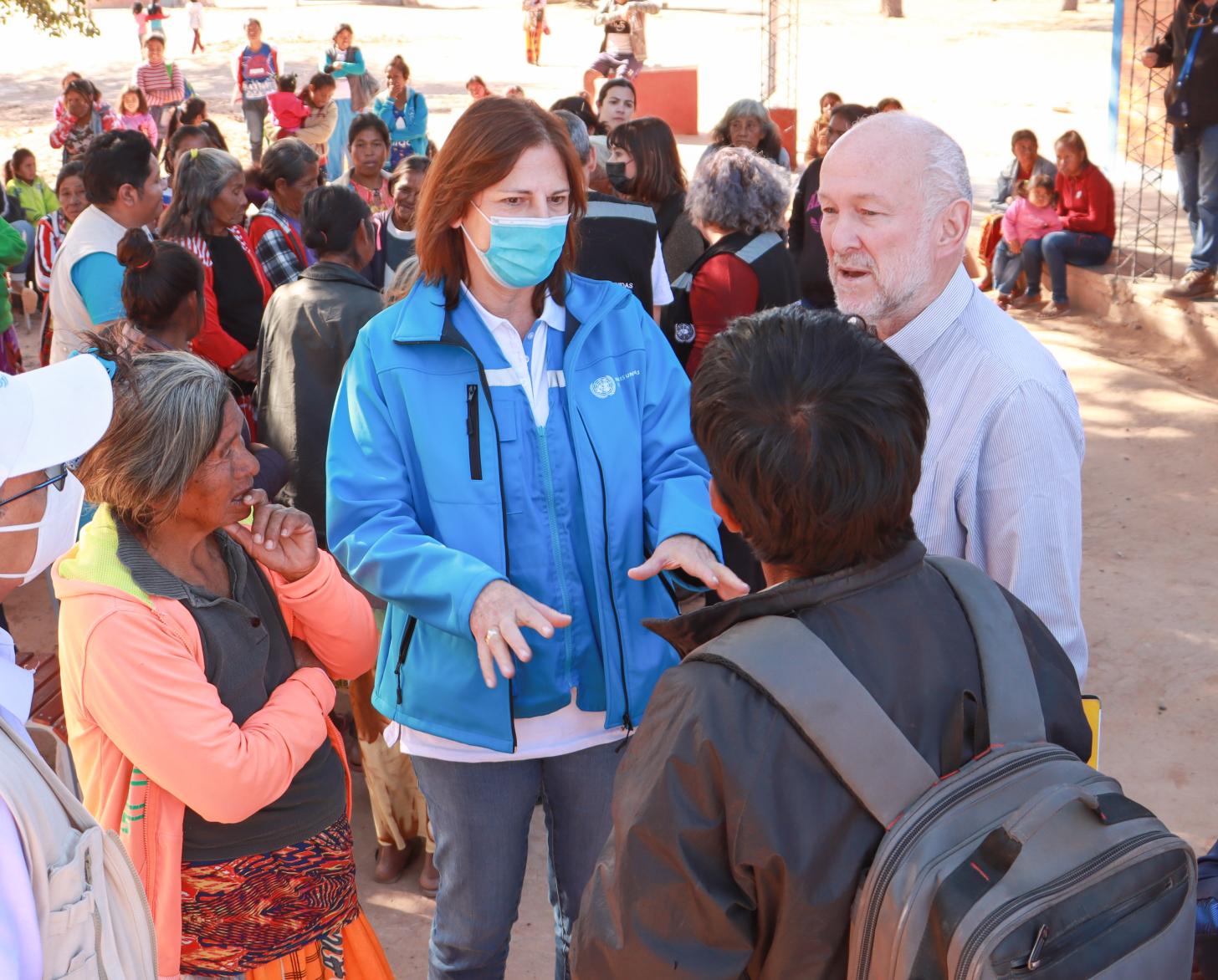 Rodeados de un grupo de personas con mascarillas, Susana Sottoli, Coordinadora Residente de ONU Bolivia y Mario Samaja Coordinador Residente de ONU Paraguay conversan con familias en la comunidad Campo Loa en Paraguay.