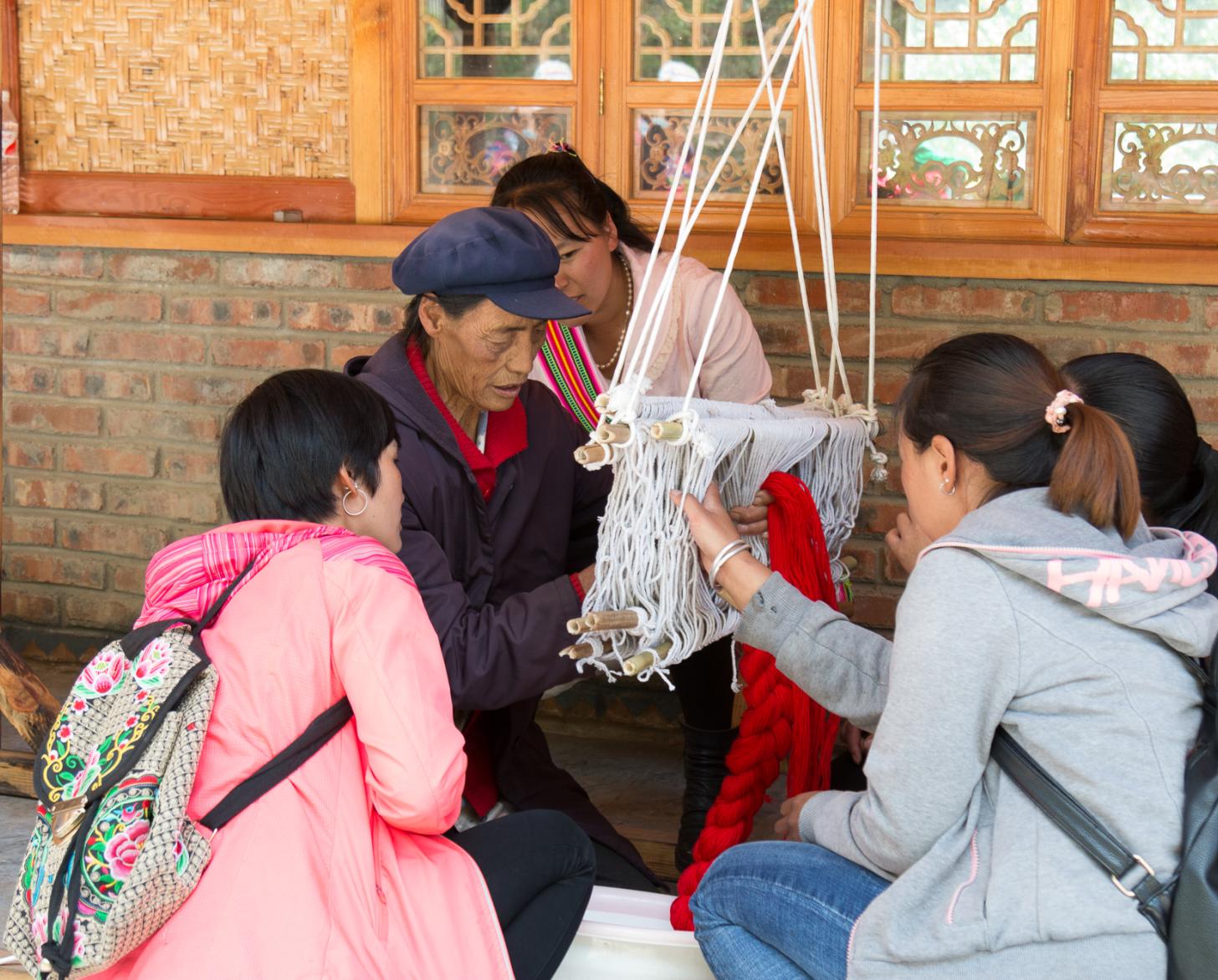 4位年轻妇女围坐在一位老妇人身边，看她编织羊毛。