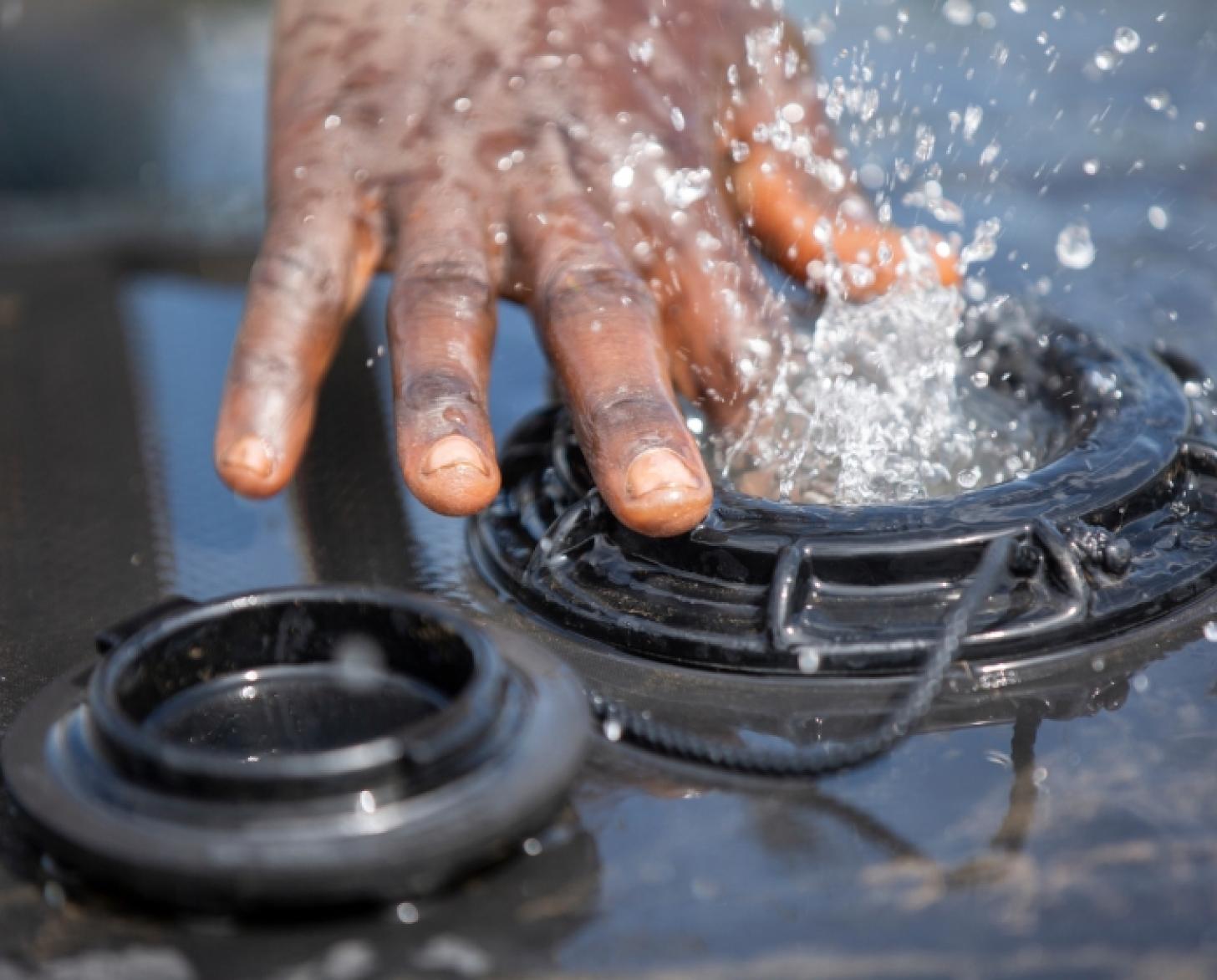 Gros plan sur la main d'un homme éclaboussée par l'eau jaillissant d'un réservoir.