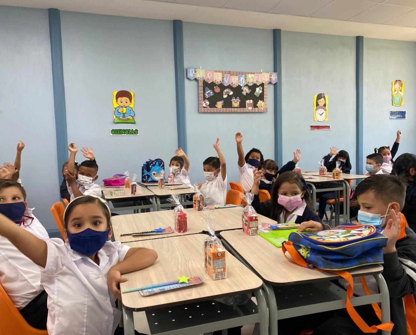 مجموعة من الأطفال يجلسون في حجرة الدراسة ويرفعون أيديهم للمشاركة في الدروس.