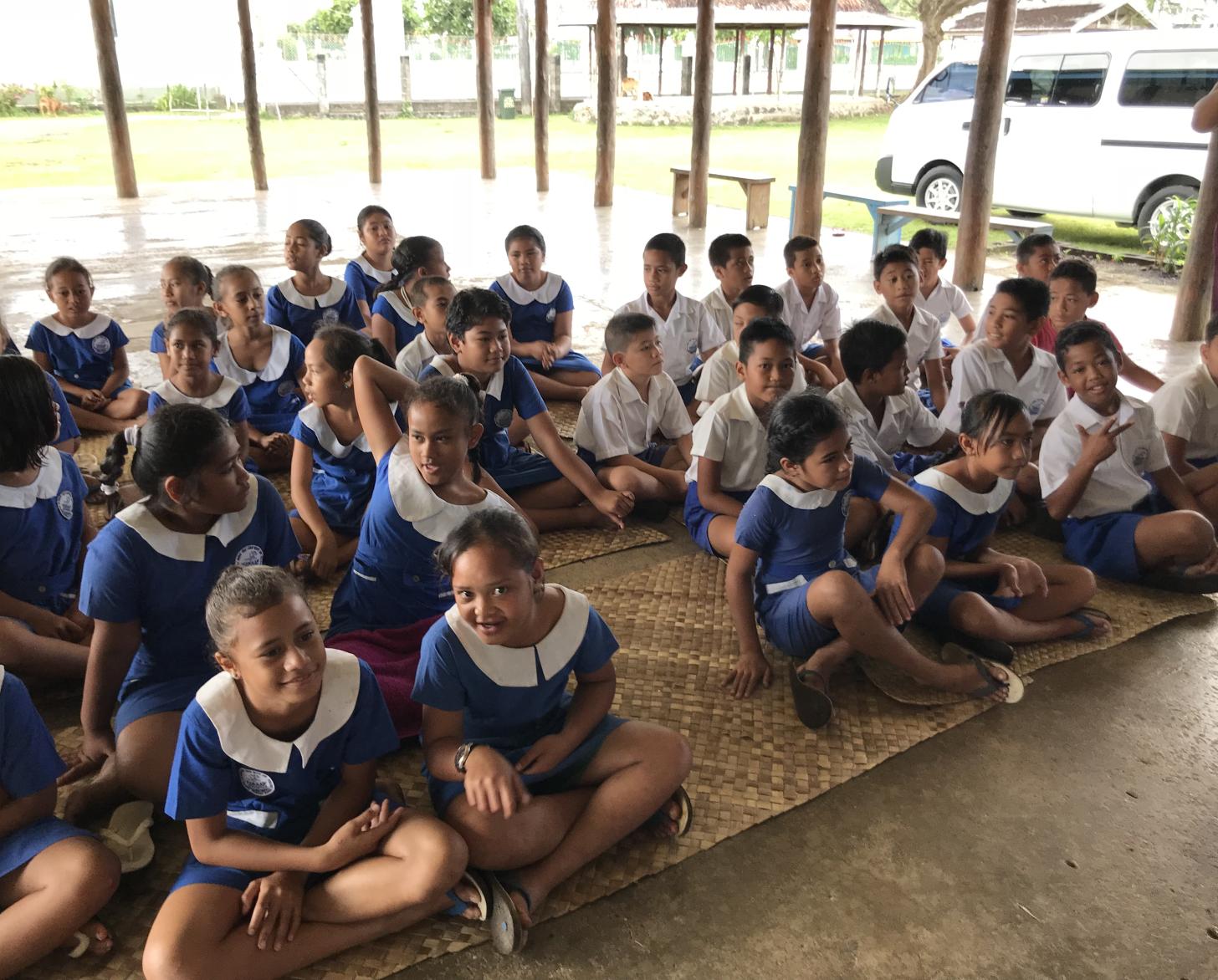 穿着校服的孩子们坐在地上的竹席上。