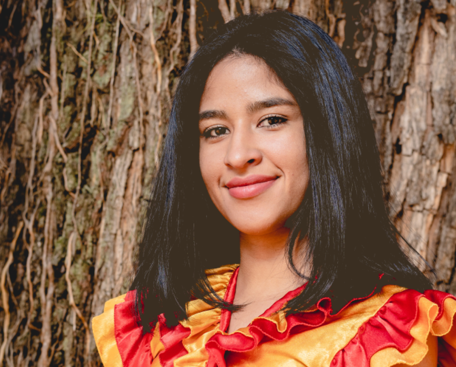 Una joven con una blusa roja y amarilla sonríe a la cámara.