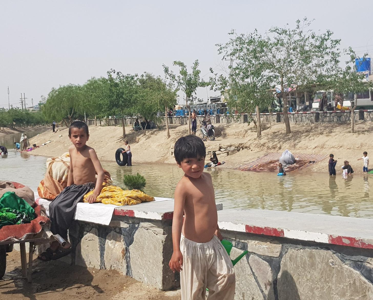 Unos niños pequeños juegan en un pequeño lago de agua rodeado de hierba y árboles de color canela.