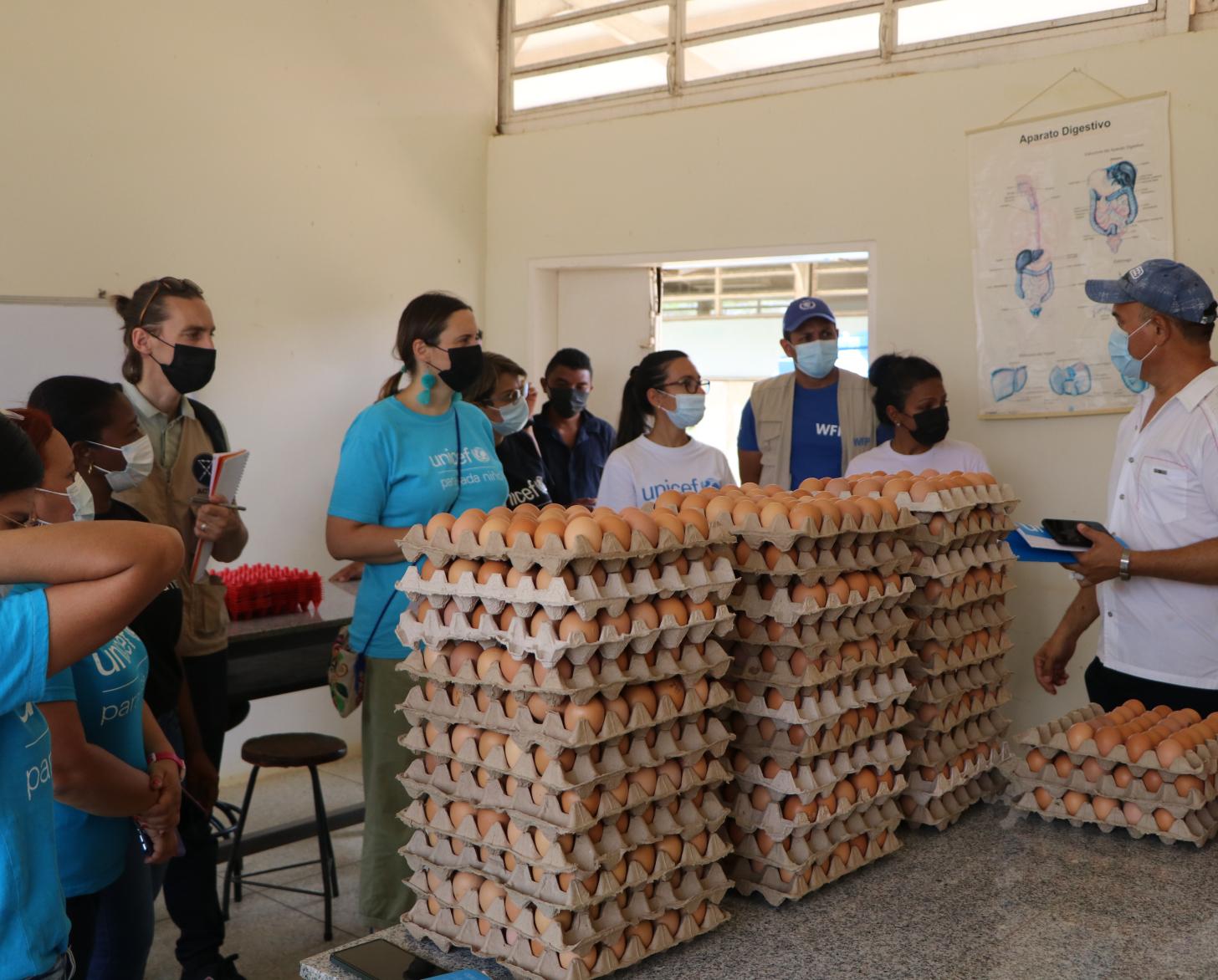 مجموعة من الأشخاص يرتدون أقنعة الوجه يتحدثون داخل مبنى المدرسة، وفي الوسط ثلاثة أبراج من البيض.