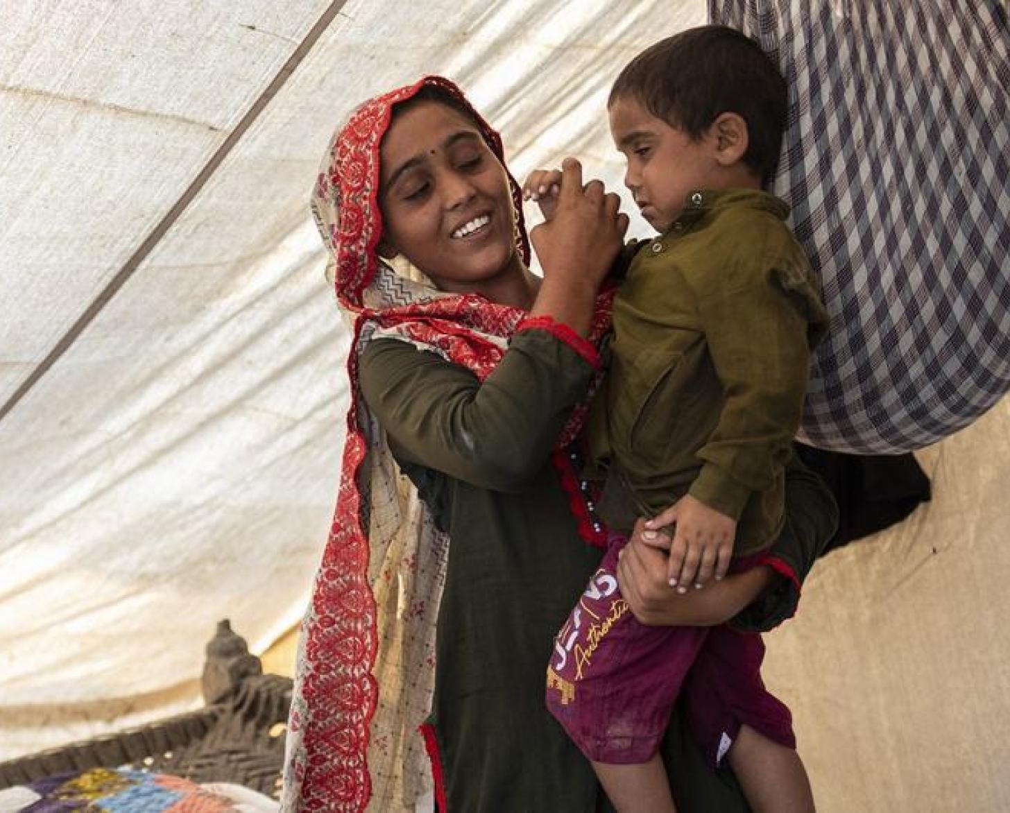 A woman in a tent-structure holds a young boy on her hip. 