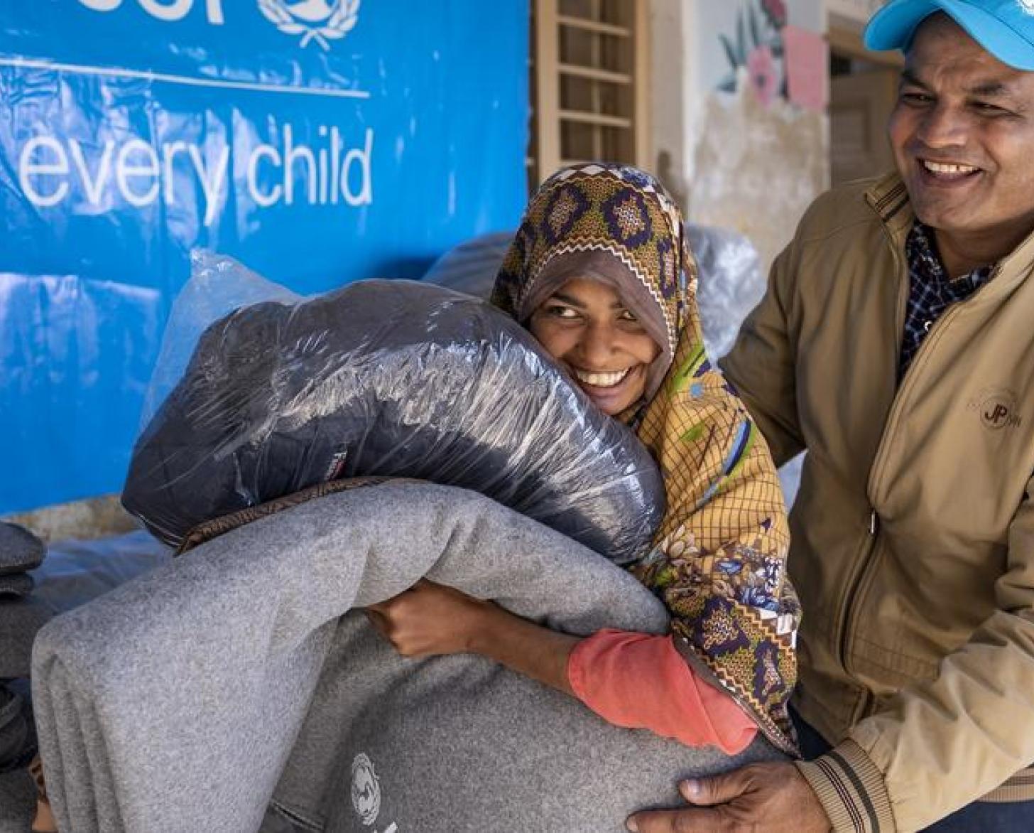 A man and a girl hold blankets and smile in front of a UNICEF sign.