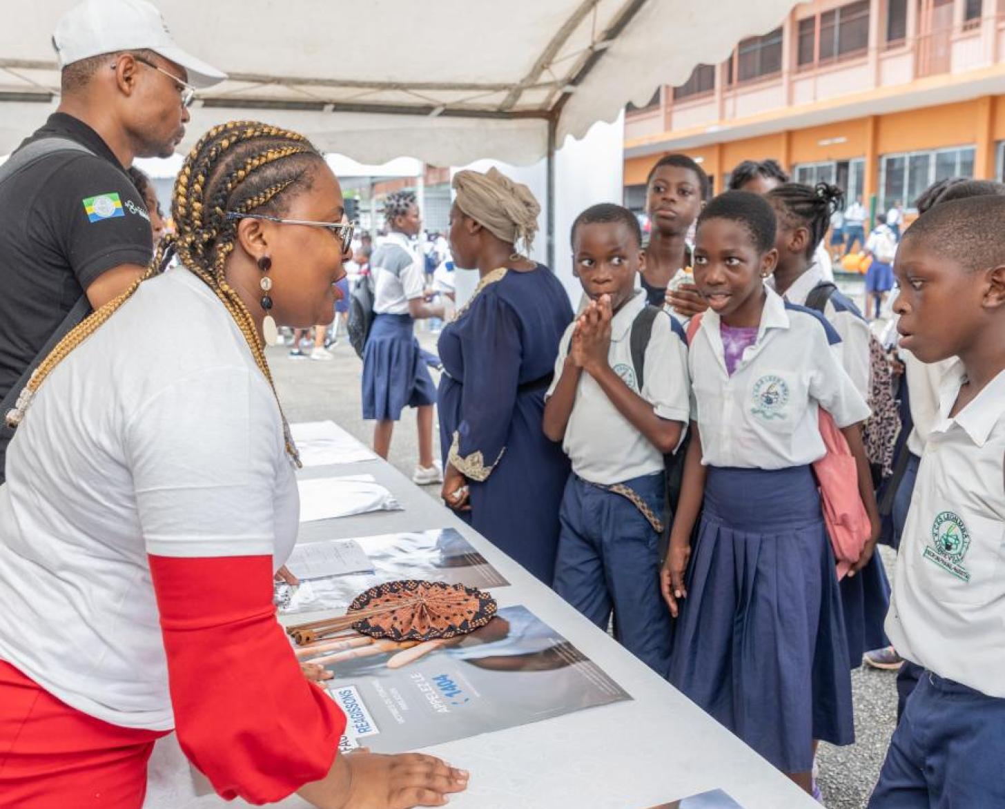 une femme en robe rouge parle à des écoliers autour d'une table
