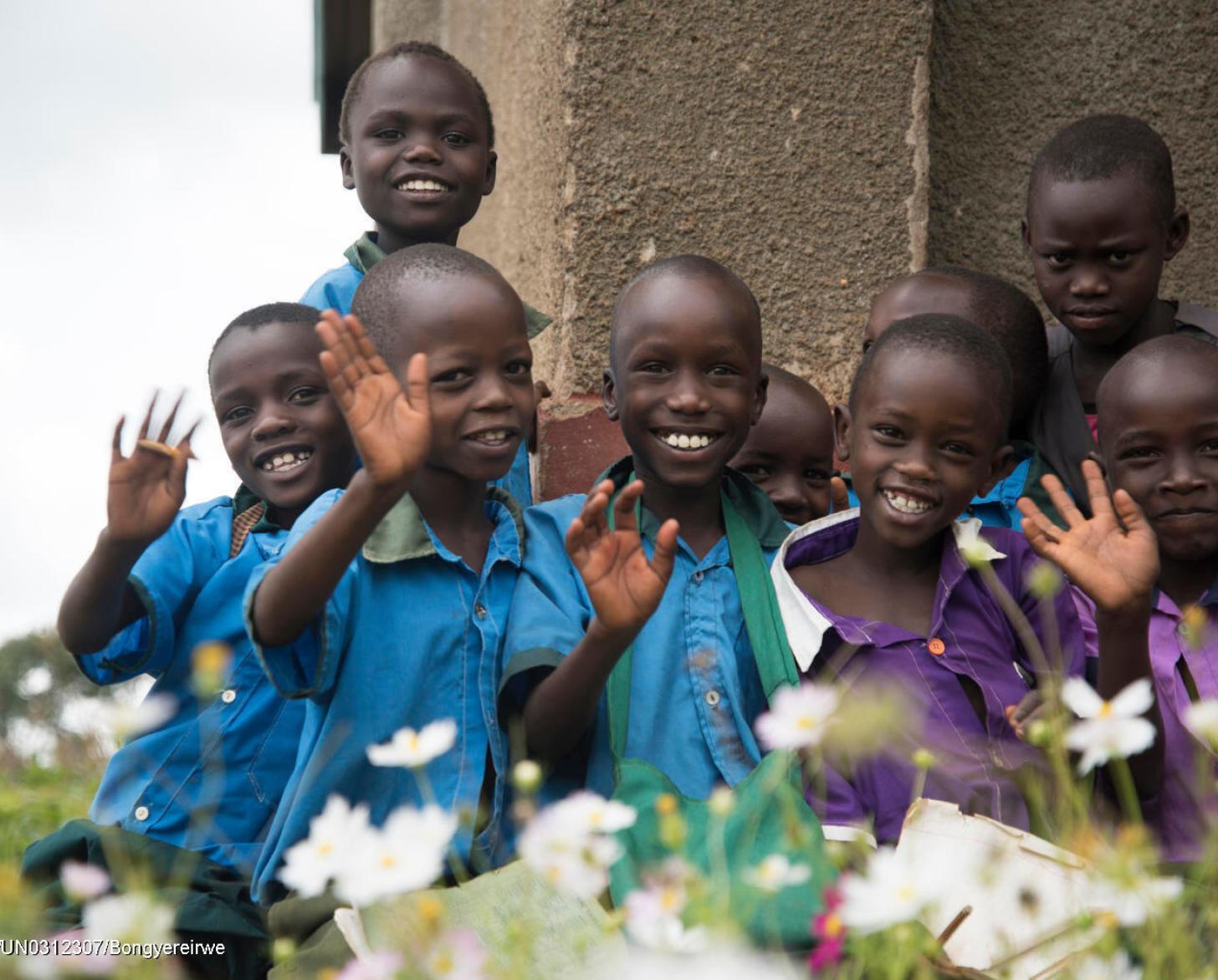 group of young school boys in blue and purple shirts stand together and wave at the camera