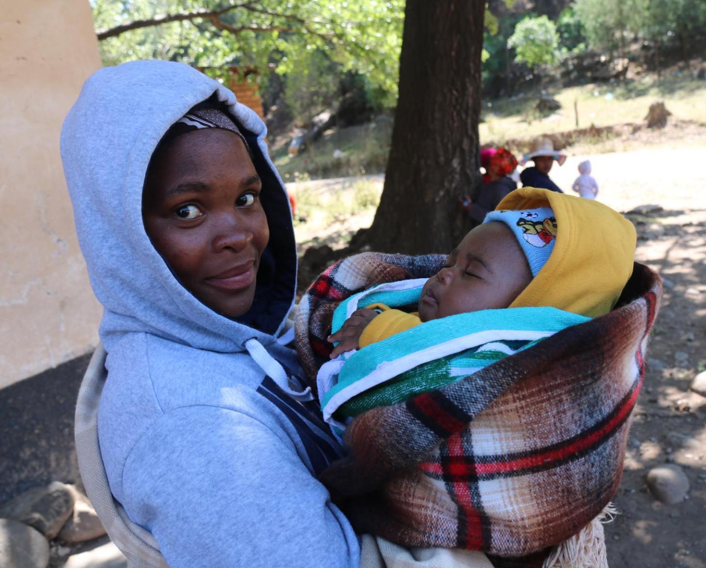 A woman is holding her baby and looking at the camera