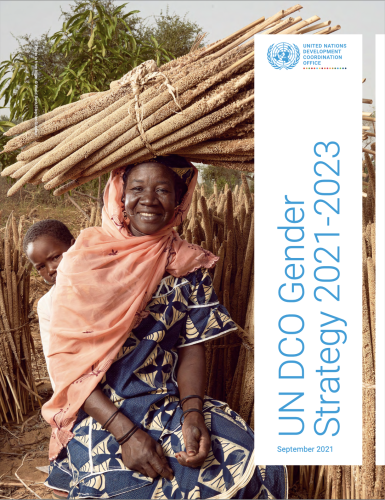 Una mujer, que carga una pila de madera, está sentada en un terreno exterior y sonríe a la cámara.