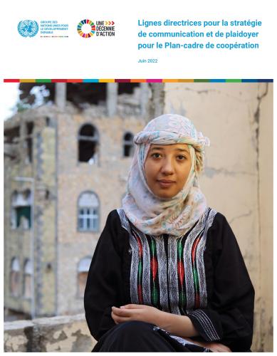 Portrait d'une jeune femme portant un fouloir autour de la tête, les bras croisés, posant devant la caméra, avec en arrière plan un bâtiment délabré.