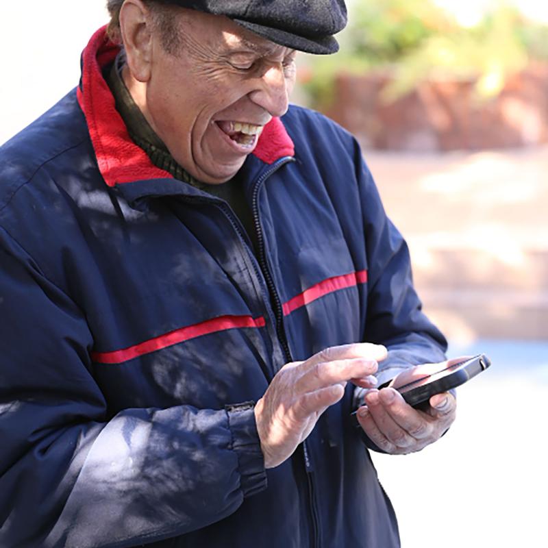 رجل يرتدي قبعة سوداء ومعطفًا أزرق يبتسم وهو ينظر إلى هاتفه الخلوي.